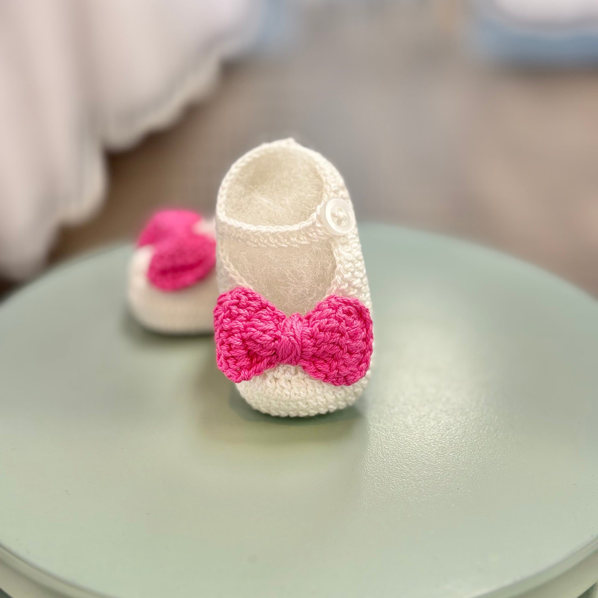 White crochet baby booties with pink bow.
