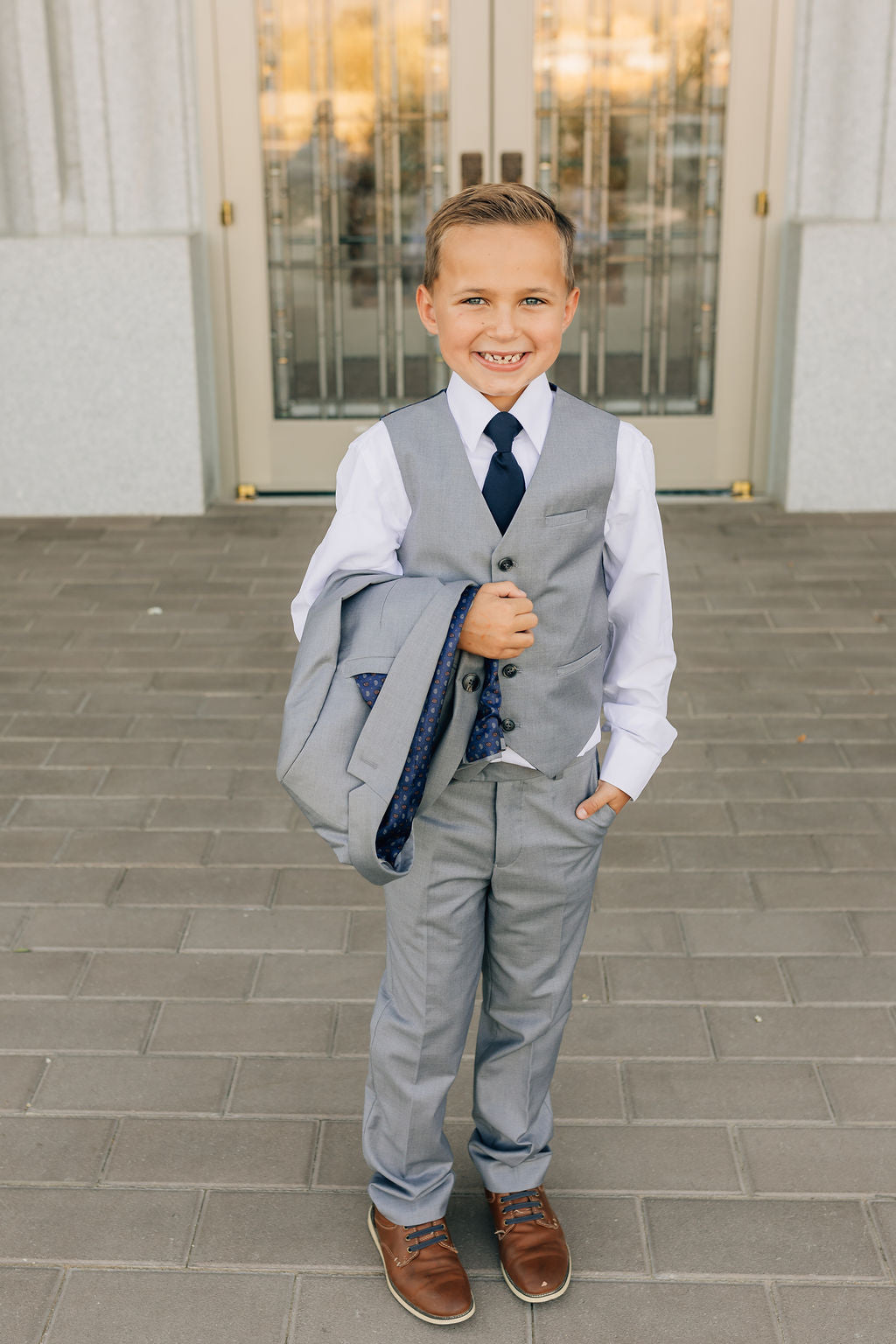 boy in gray suit with coat over arms